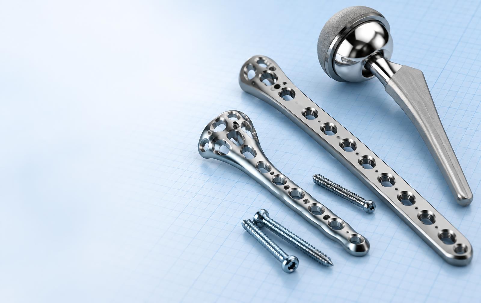 Stainless steel hip stem, locking plates and screws on blue graph paper